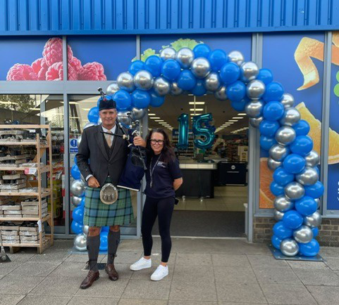 A store manager stands with a bagpiper outside Company Shop Corby.