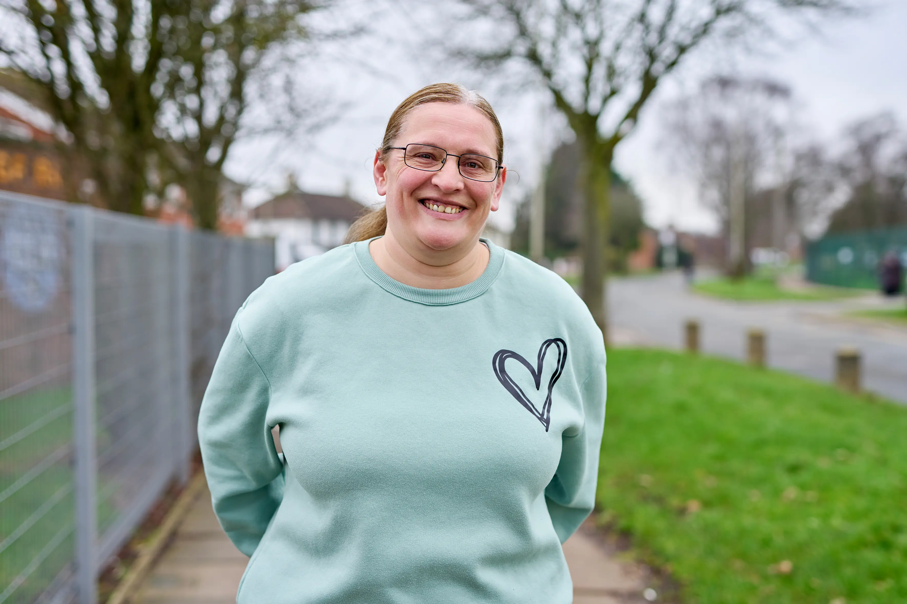 Kate, a Community Shop Stocking Farm member is wearing a blue love heart jumper andsmiles in her local estate