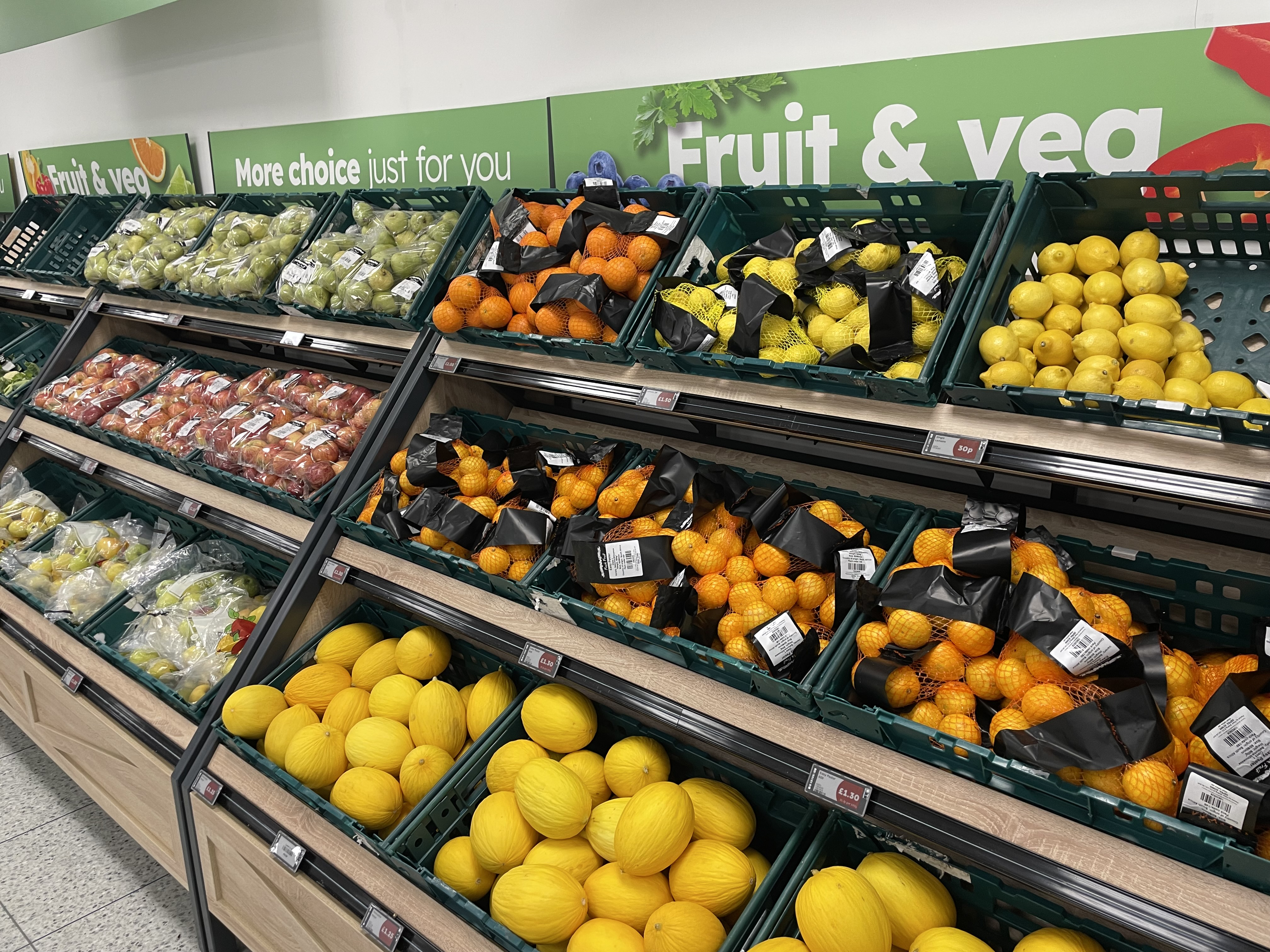 Shelves of lemons, oranges, melons and apples underneath signs that read Fruit & Veg.