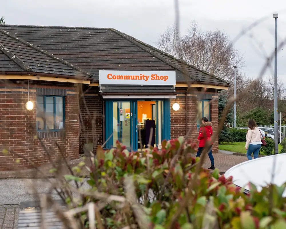Two women walking into a well lit building with a sign saying Community Shop.