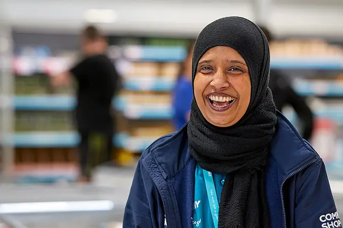 A Company Shop employee wearing her uniform and a black headscarf smiles at the camera.