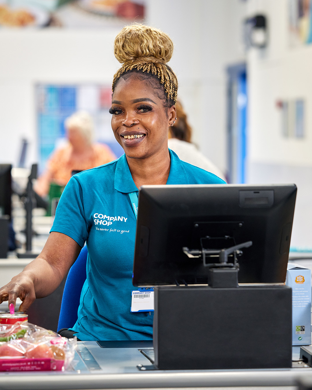 A woman of colour with vibrant pink nails operates a till at a Company Shop.