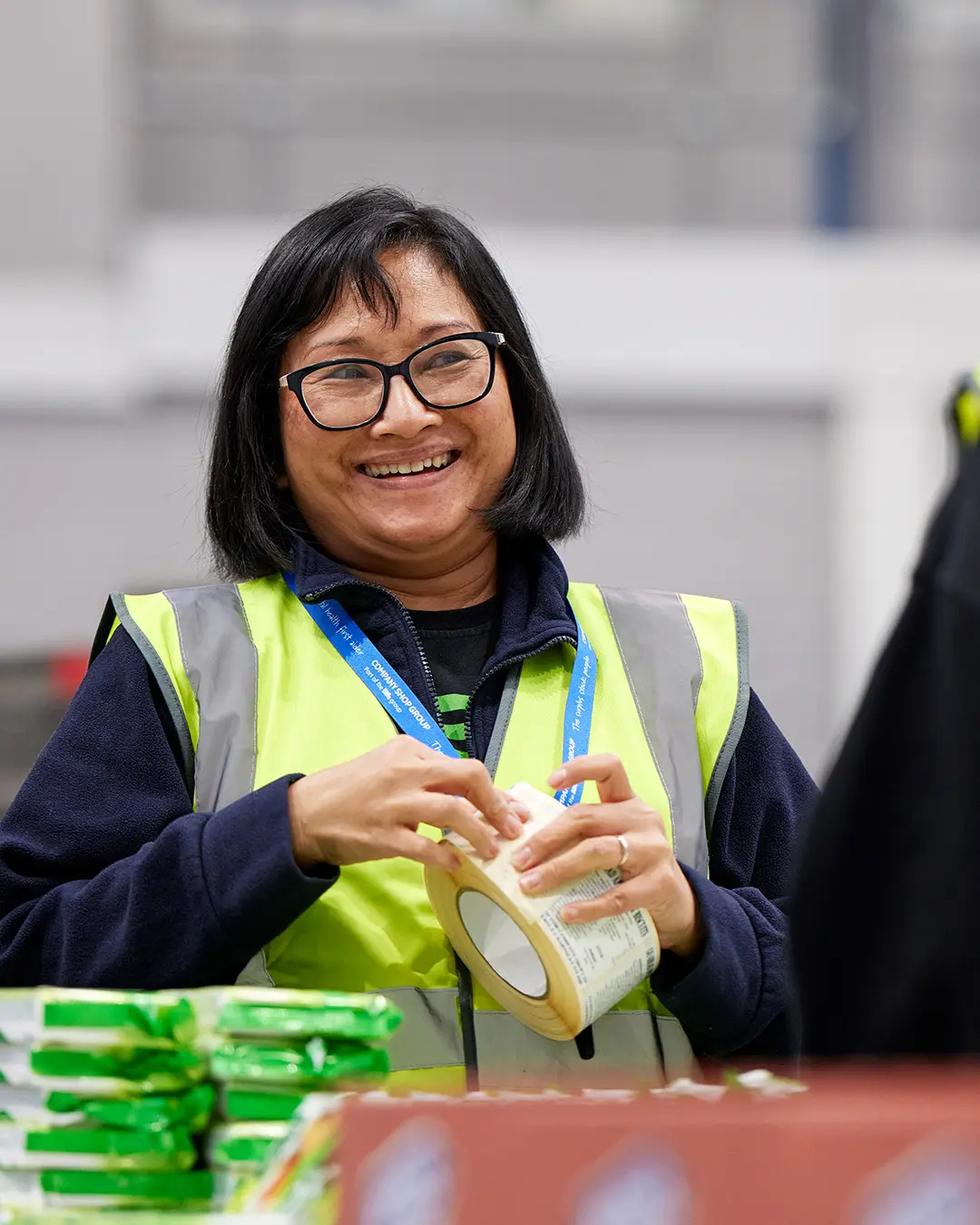 Female Company Shop Group warehouse operative wearing PPE, smiles as she peels off a label.