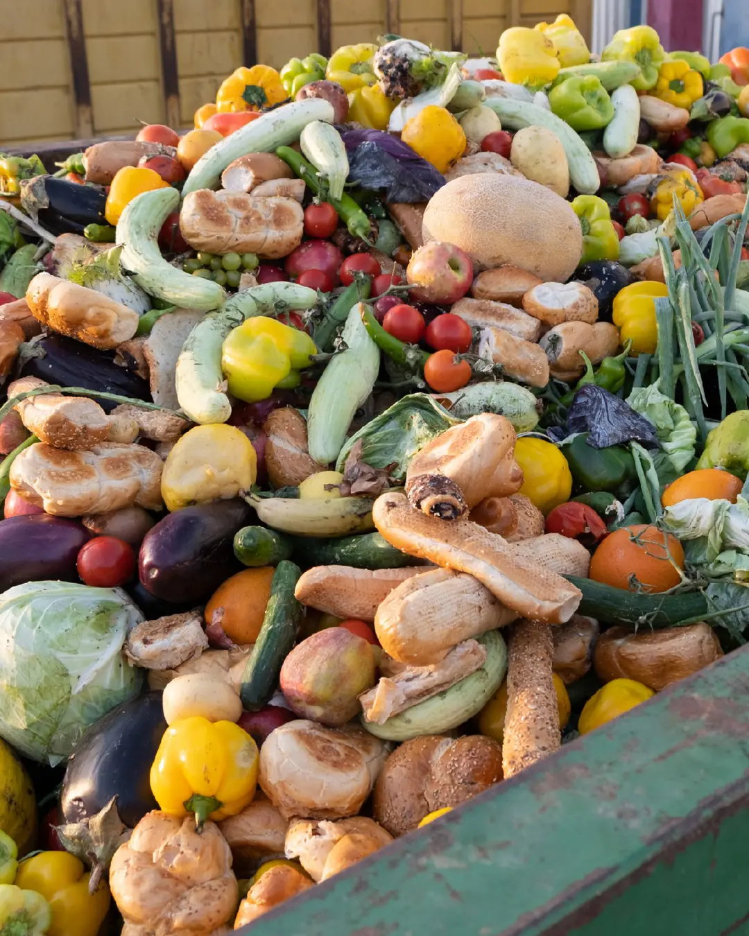 A green skip filled with fruit, vegetables and bread.