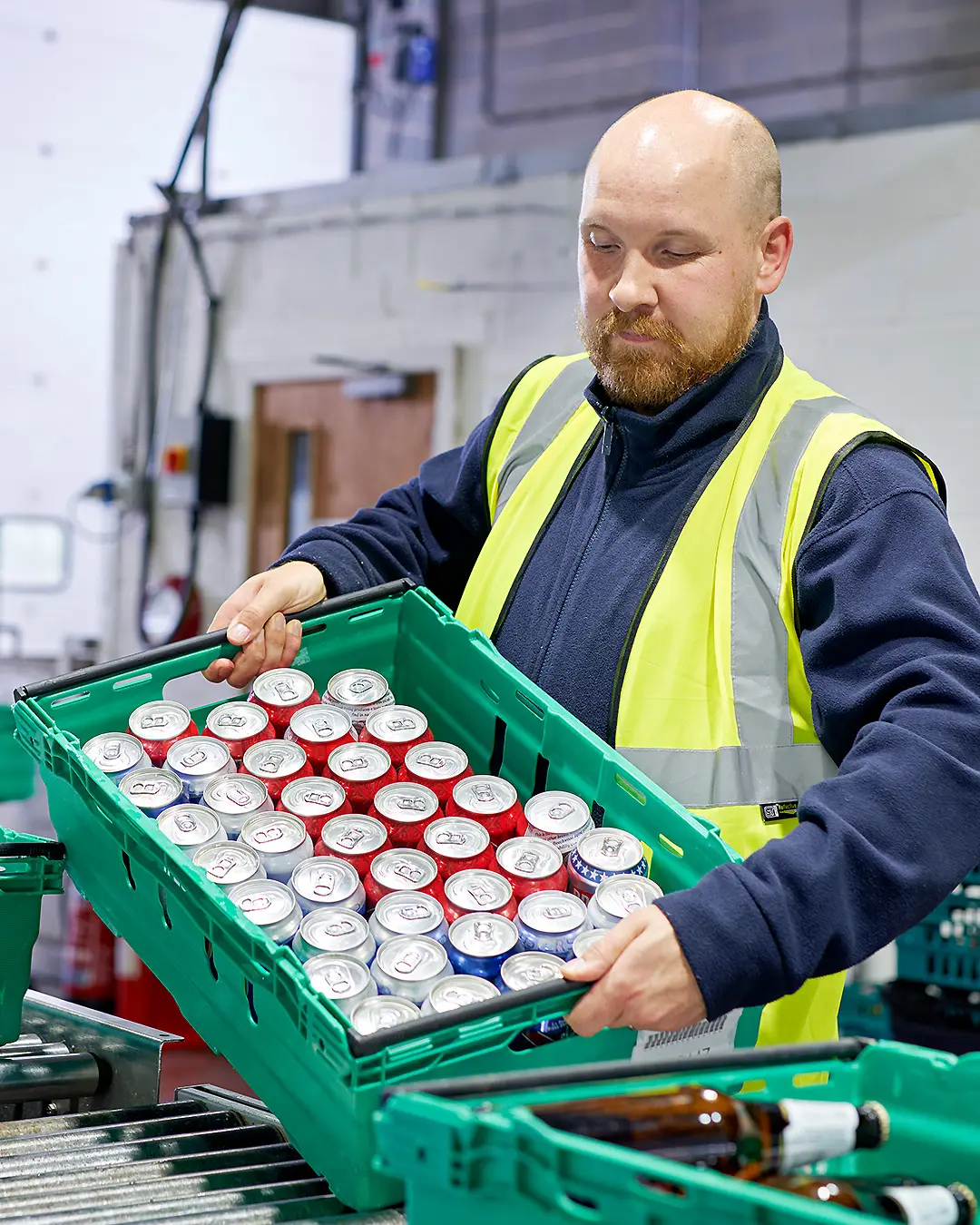 A man carefully loads a crate of beer cans onto a conveyor belt, ready to be washed in a state-of-the-art bottle washing facility.