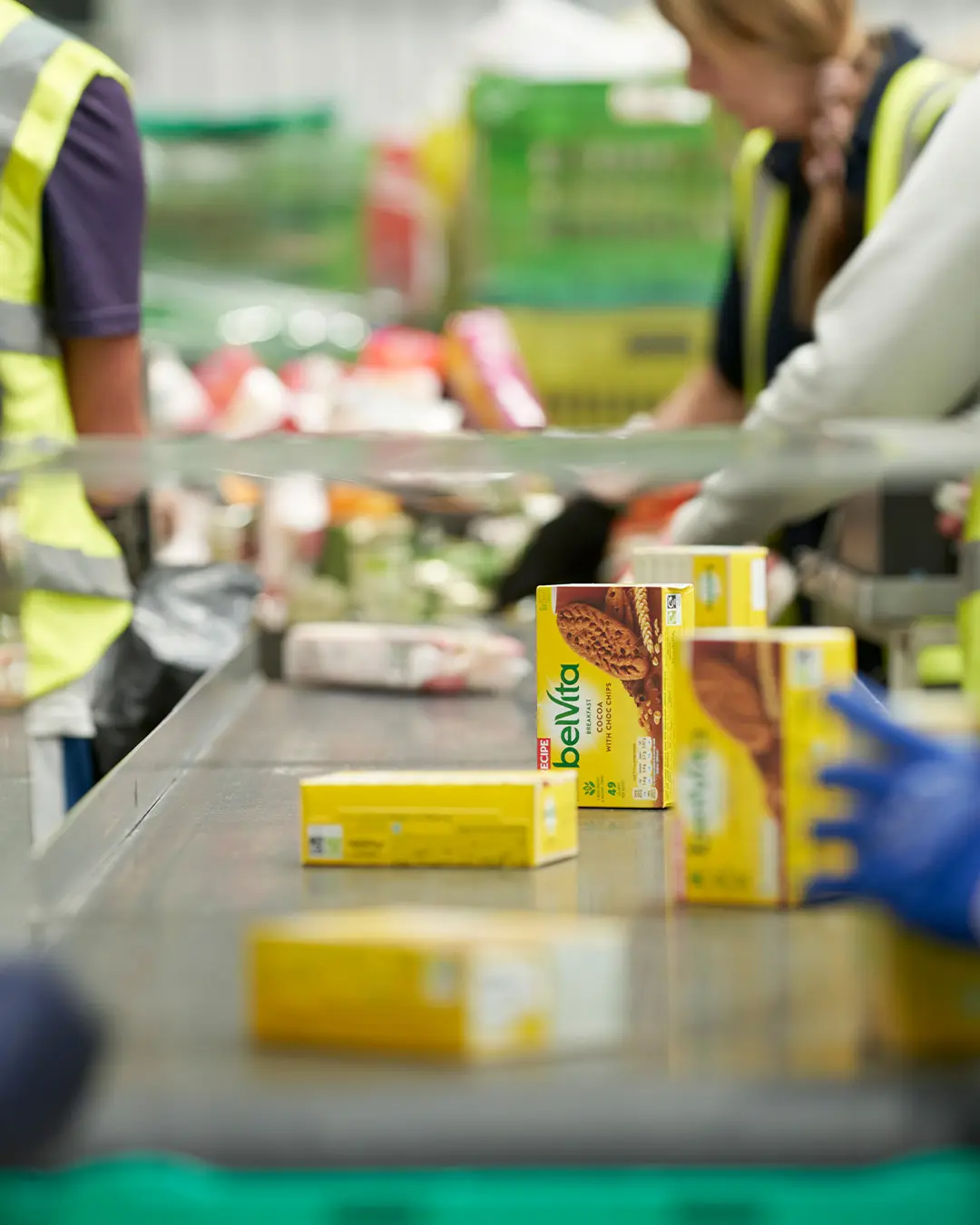 Warehouse operatives moving surplus boxes of belvita biscuits along a conveyor belt.