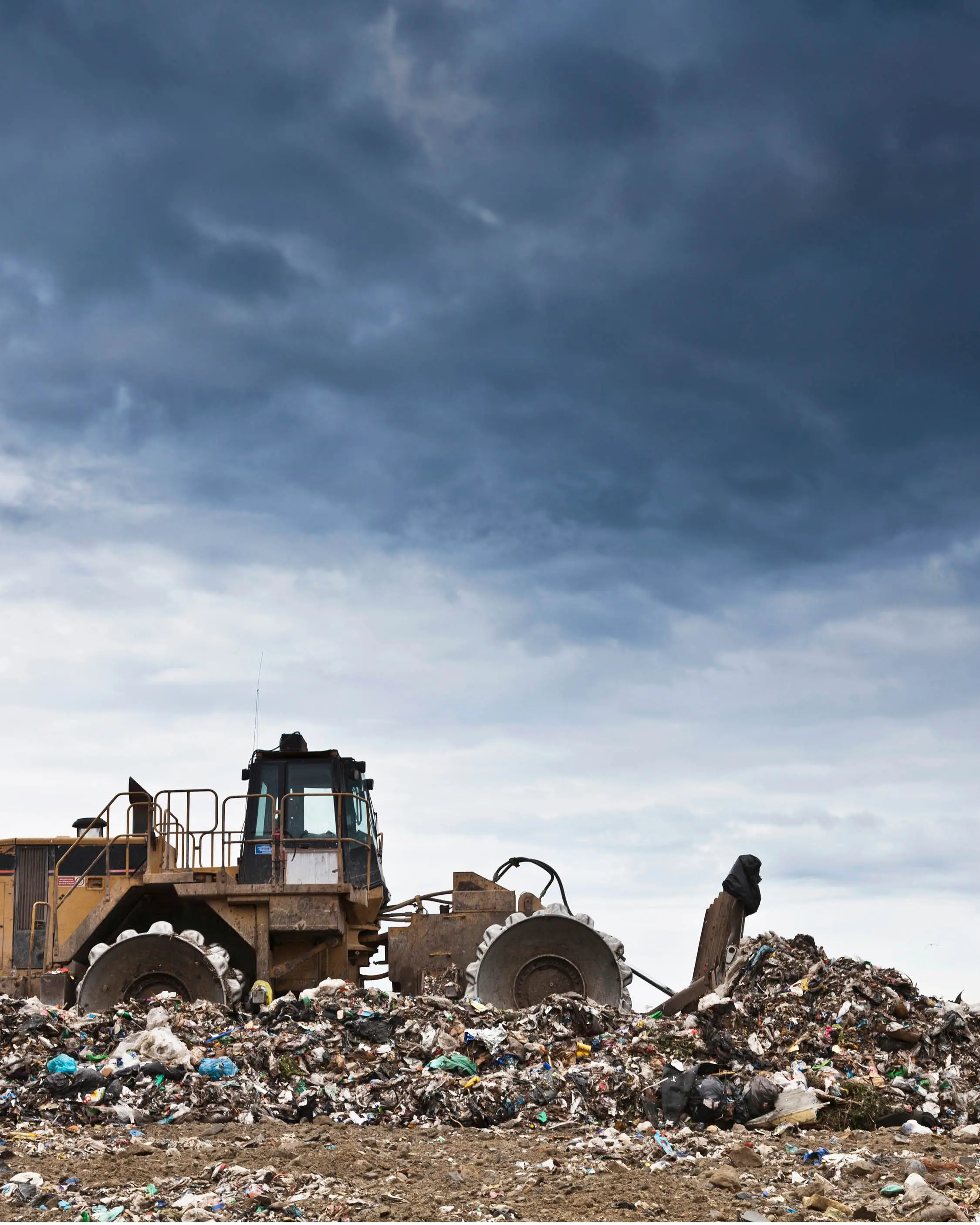 A landfill compactor moves rubbish across a landfill on a dark, overcast day.