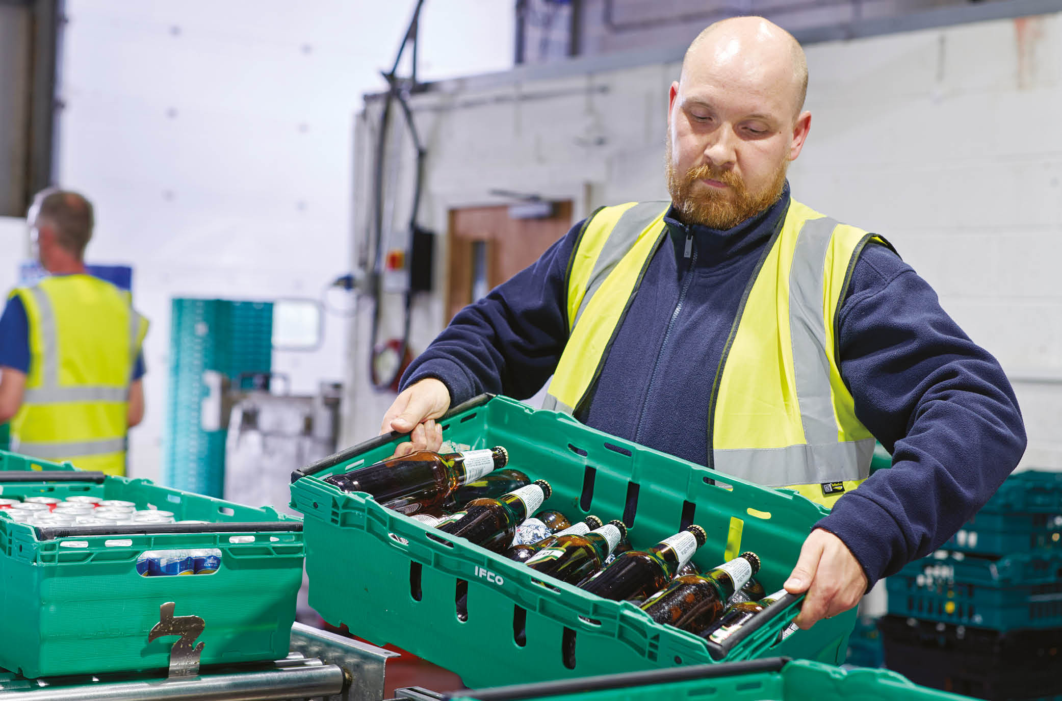A man carefully loads a crate of beer cans onto a conveyor belt, ready to be washed in a state-of-the-art bottle washing facility.