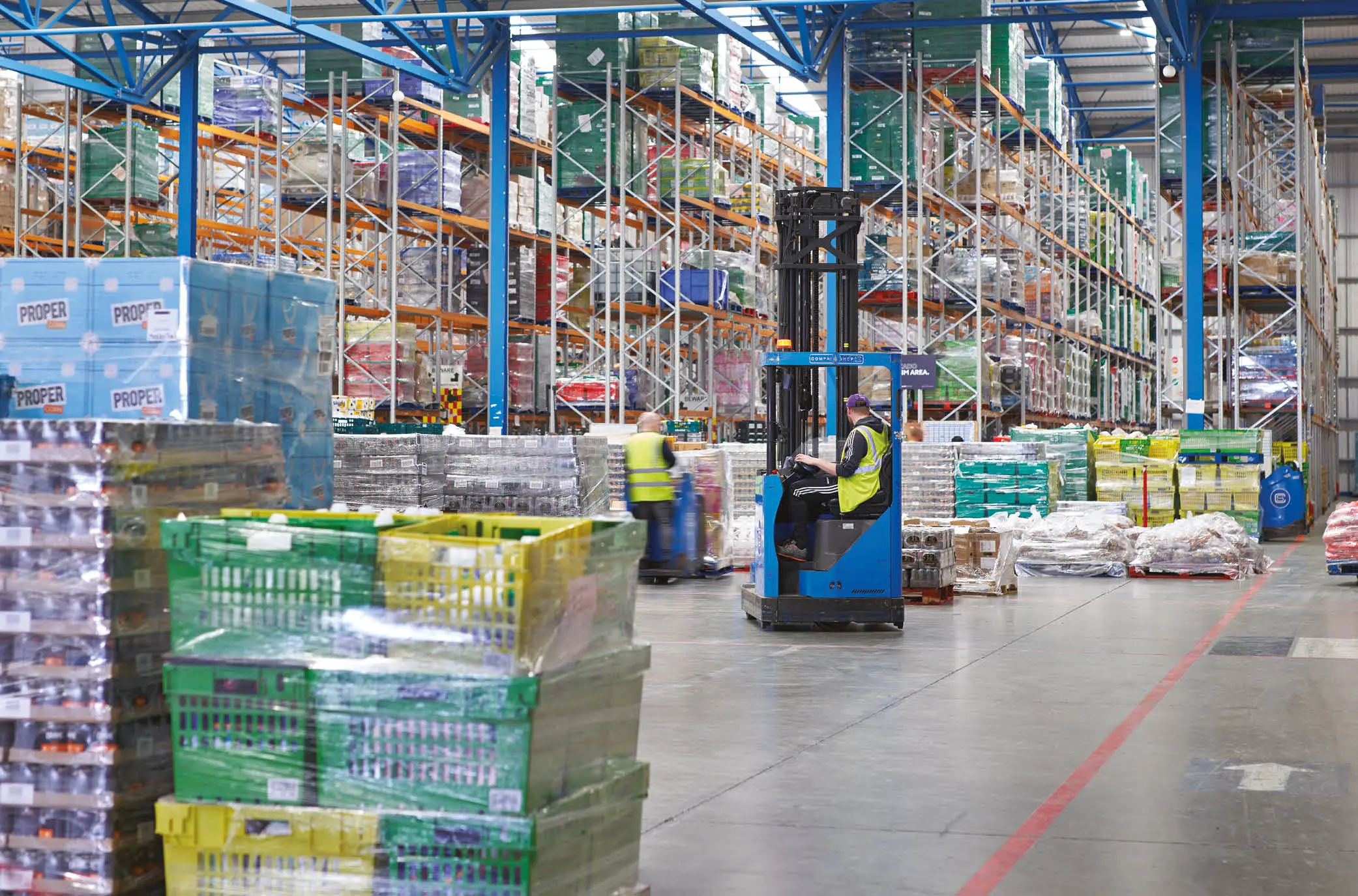 A man wearing a high vis is operating a forklift in a fully stocked Company Shop Group surplus warehouse.