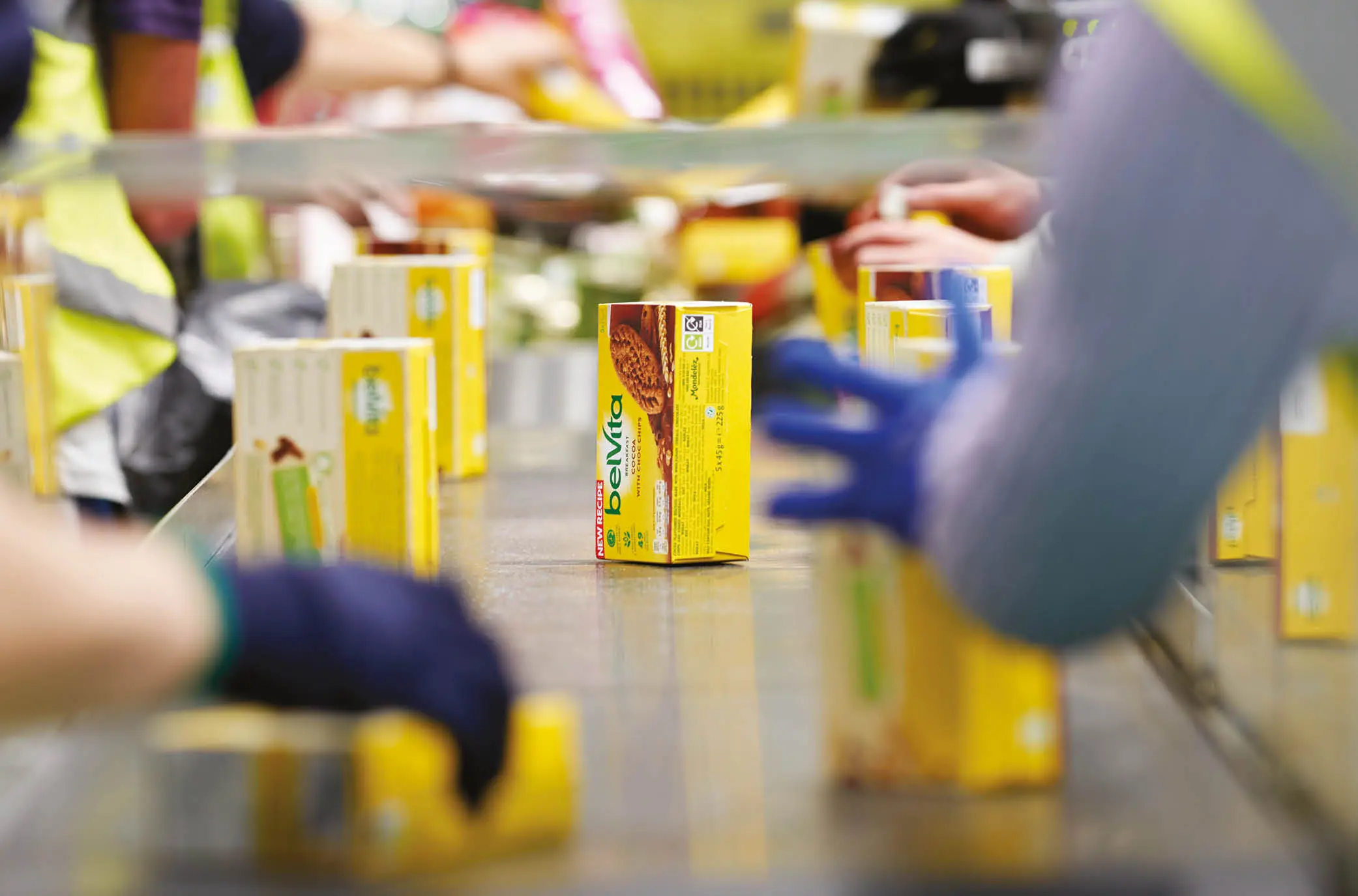 Warehouse operatives moving surplus boxes of belvita biscuits along a conveyor belt.