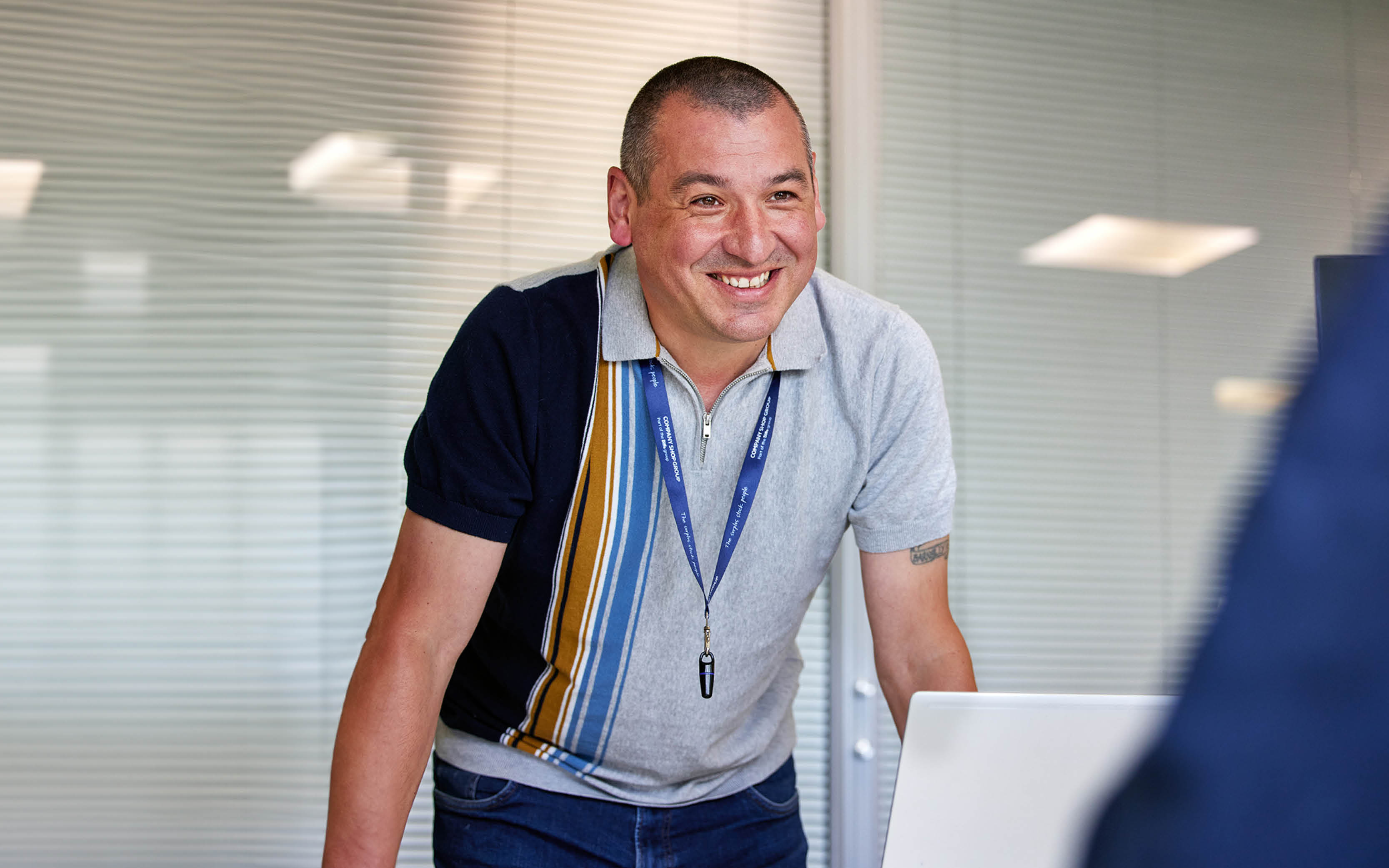 A man wearing a Company Shop Group lanyard smiles as he welcomes an interviewee.